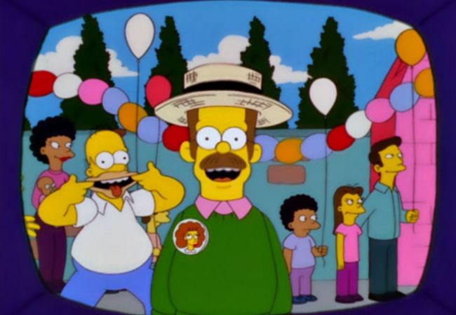 Ned Flanders gibt ein TV-Interview. Im Hintergrund zieht Homer Grimassen.